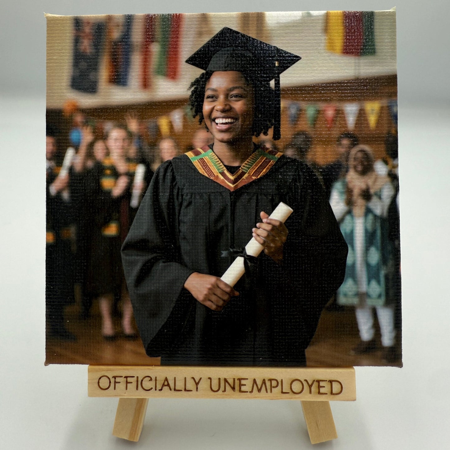 Graduating student in cap and gown holding a diploma with 'Officially Unemployed' sign below.